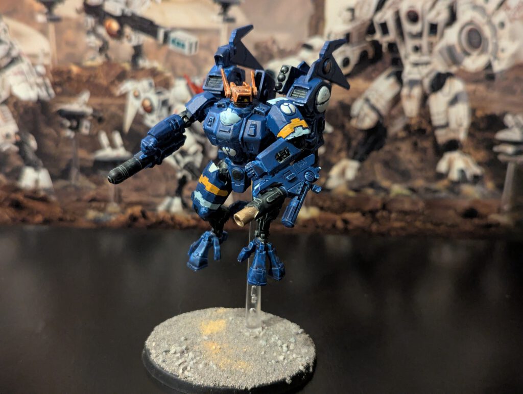 Painted T’au Commander in Enforcer Battlesuit, shown from a top-front angle with full weapon loadout visible.