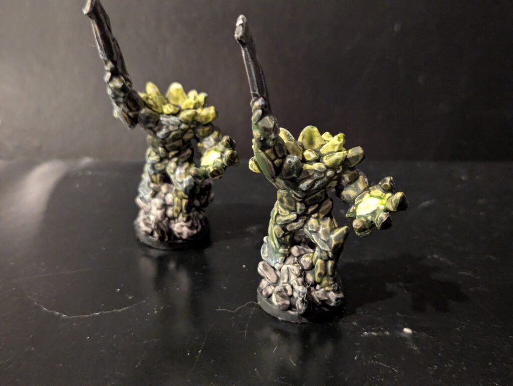 Two Earth Loa figures painted with rocky, earthen textures and mossy green highlights.