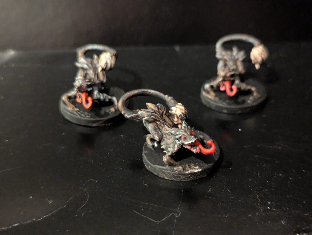 Three Merk Hound miniatures painted with snarling expressions and dark, monstrous fur tones.