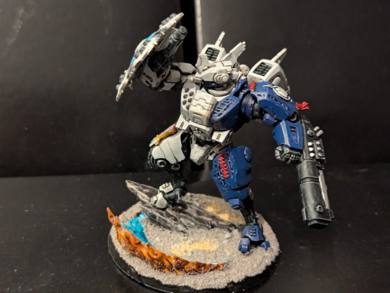 Side view of a T'au Crisis suit in a dynamic pose, showing the weapon arm and shoulder sensors.