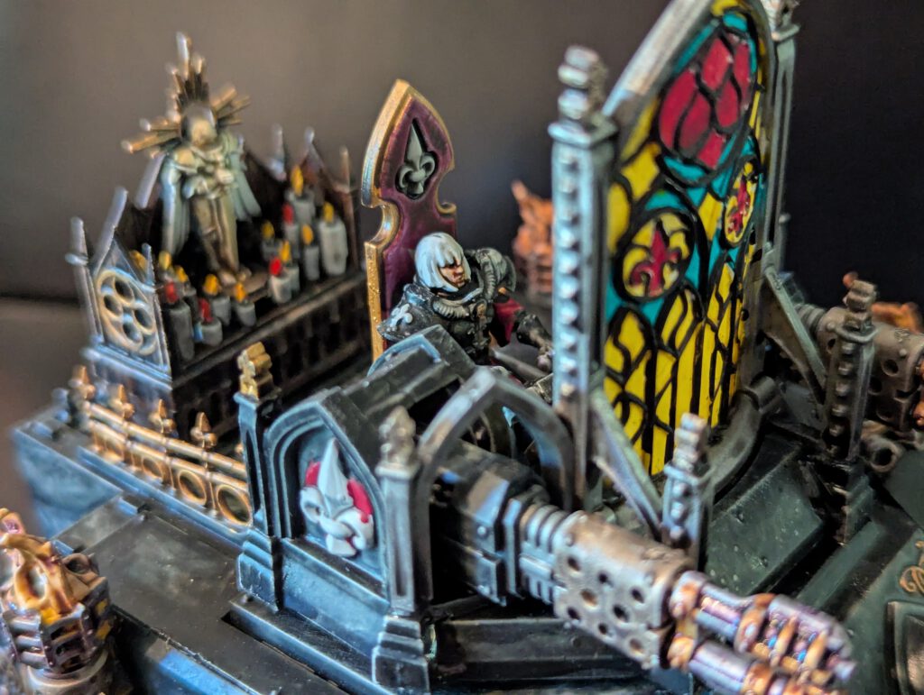 Close-up of the Immolator cockpit showing the Sister of Battle driver and the intricate painted details of the gothic stained-glass window.